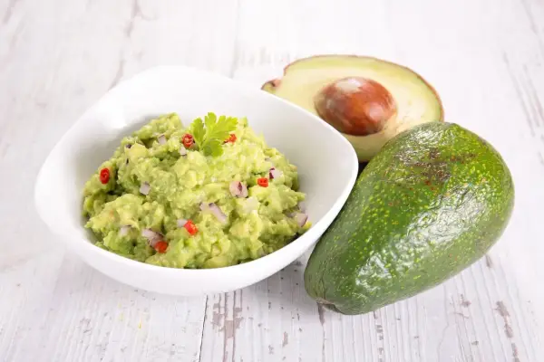 Miseczka guacamole z awokado, cebulą i papryczką chili na drewnianym tle.
